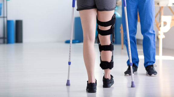 Person on crutches with leg brace in physical therapy